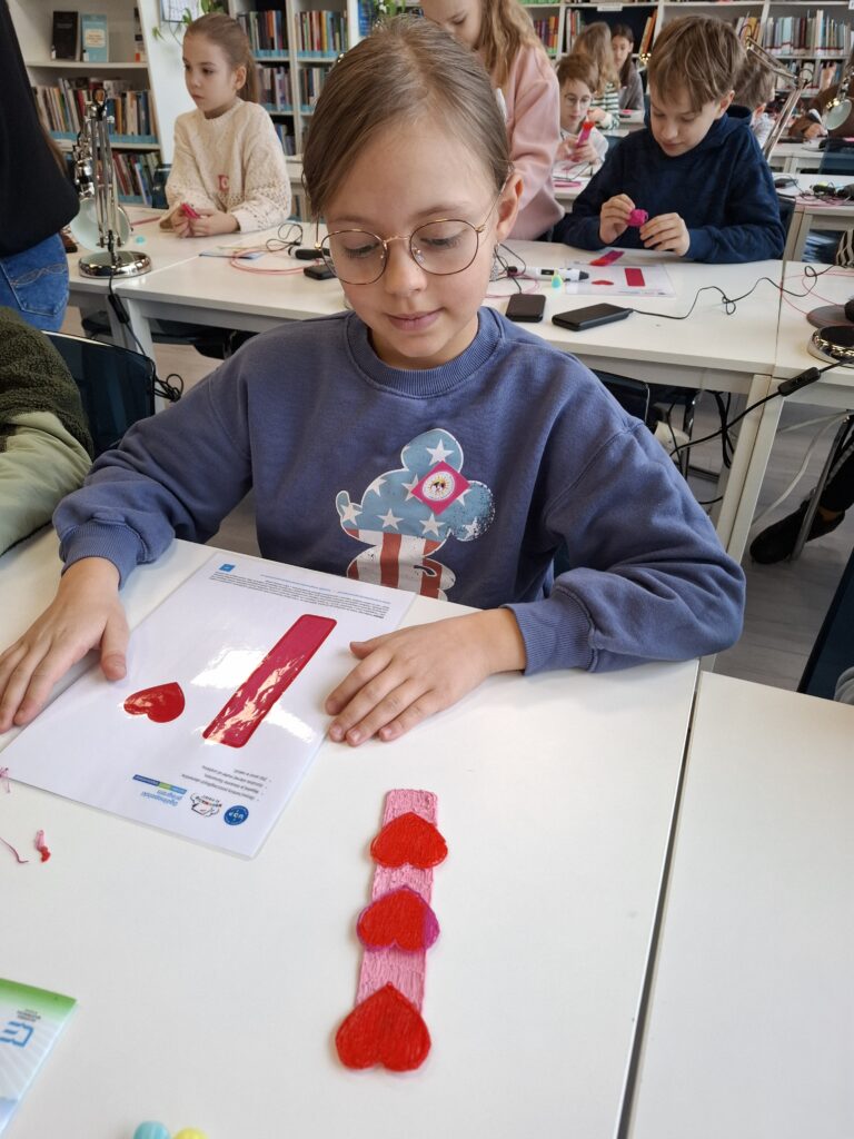 Dziewczynka patrzącą z zachwytem na wykonaną przez siebie zakładkę do książki za pomocą długopisu 3D.