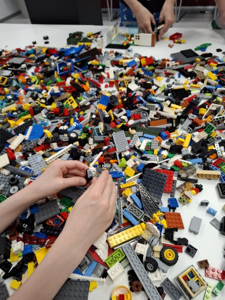 Na zdjęciu widać dzieci bawiące się klockami LEGO przy dużym białym stole.