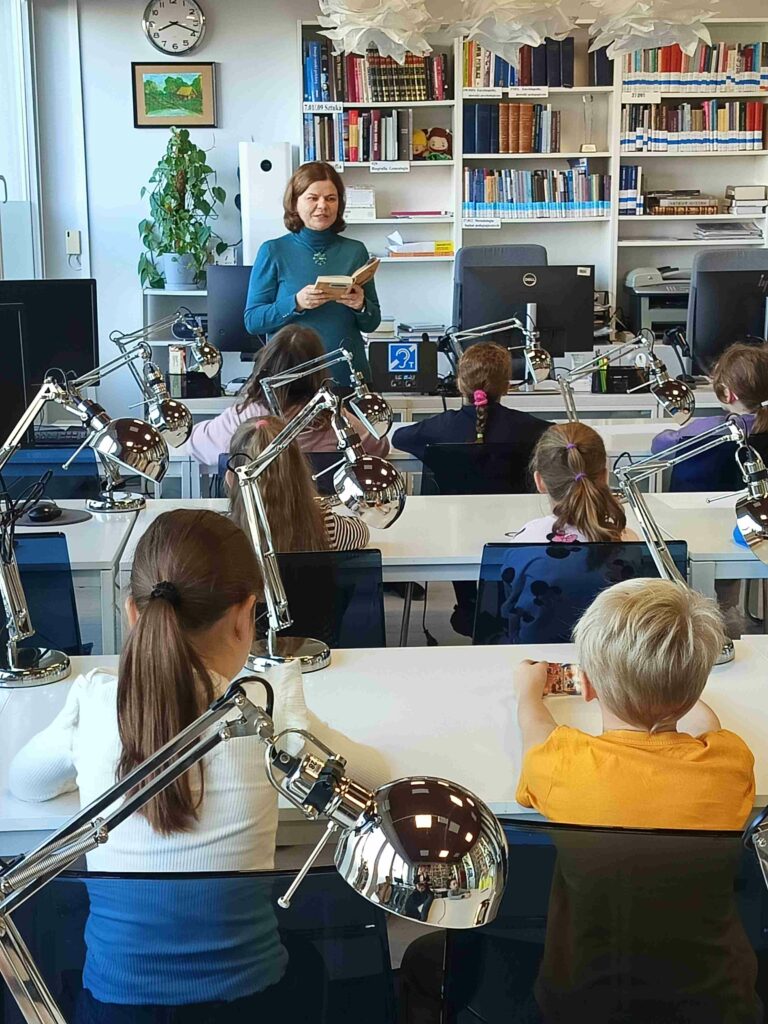 Nauczycielka w czytelni czyta dzieciom książkę.