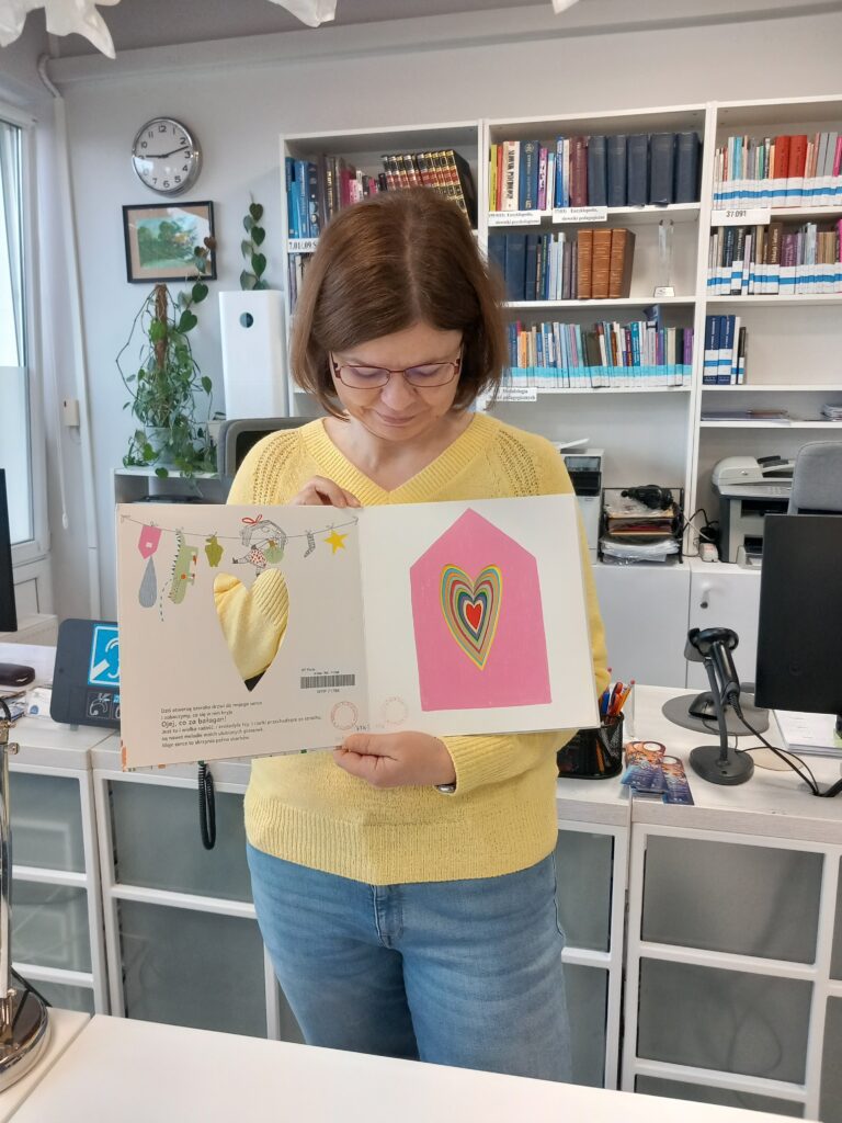 Nauczycielka w czytelni trzyma w dłoniach otwartą książkę dla dzieci