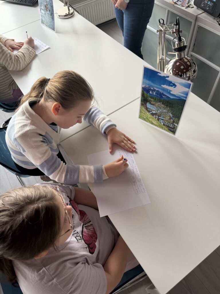 Dwie dziewczynki przy stoliku opisują zdjęcie krajobrazu