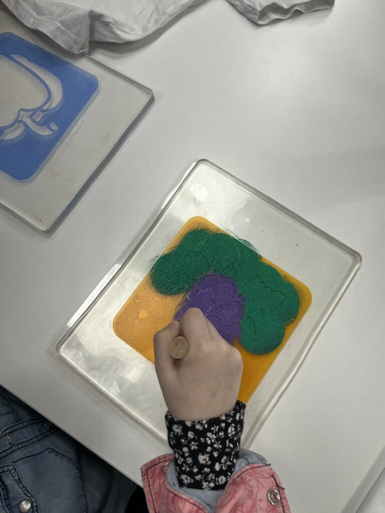 Na zdjęciu widać dziecko odbijające wzór winogrona farbą na przezroczystej płytce.