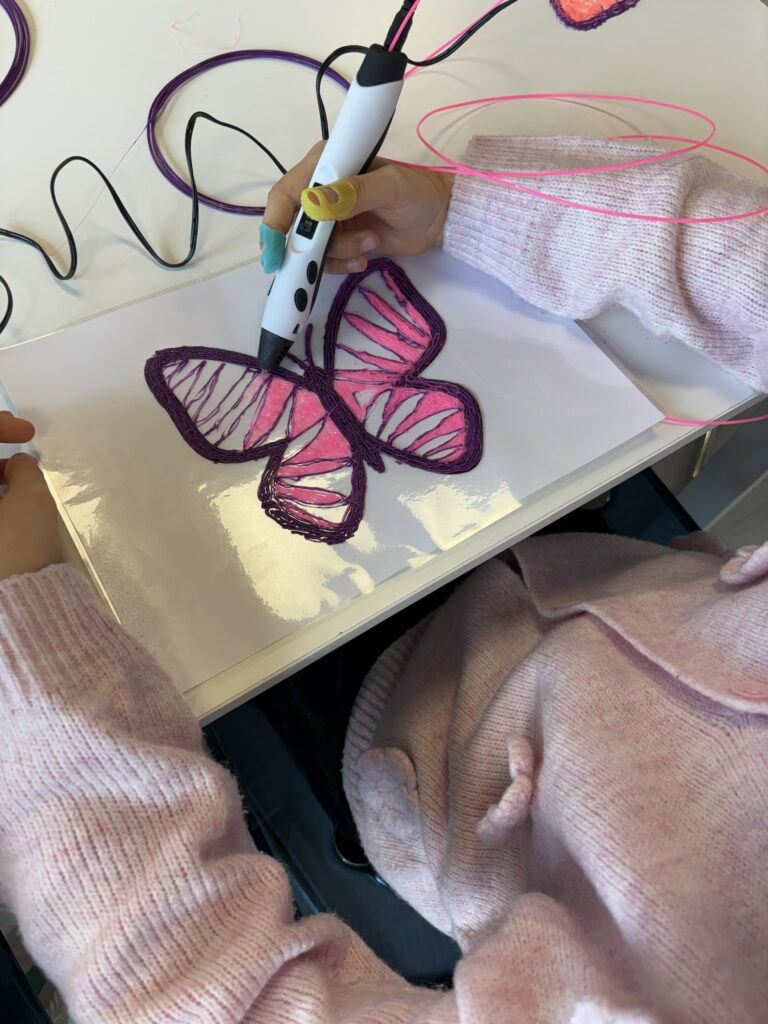 Na zdjęciu widać dziecko tworzące motyla za pomocą długopisu 3D.