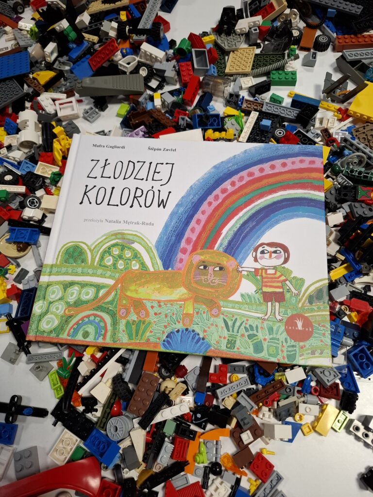 Na zdjęciu widać książkę „Złodziej kolorów” leżącą na tle rozsypanych, kolorowych klocków Lego.