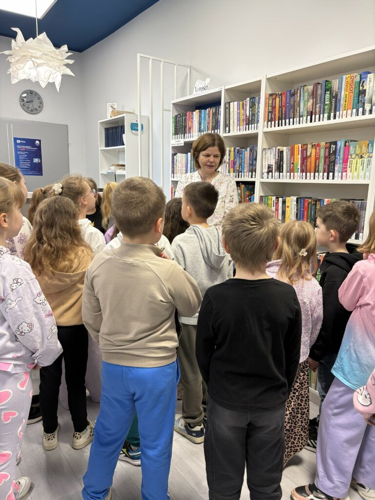 Nauczycielka z grupą dzieci z klasy pierwszej szkoły podstawowej w wypożyczalni w bibliotece