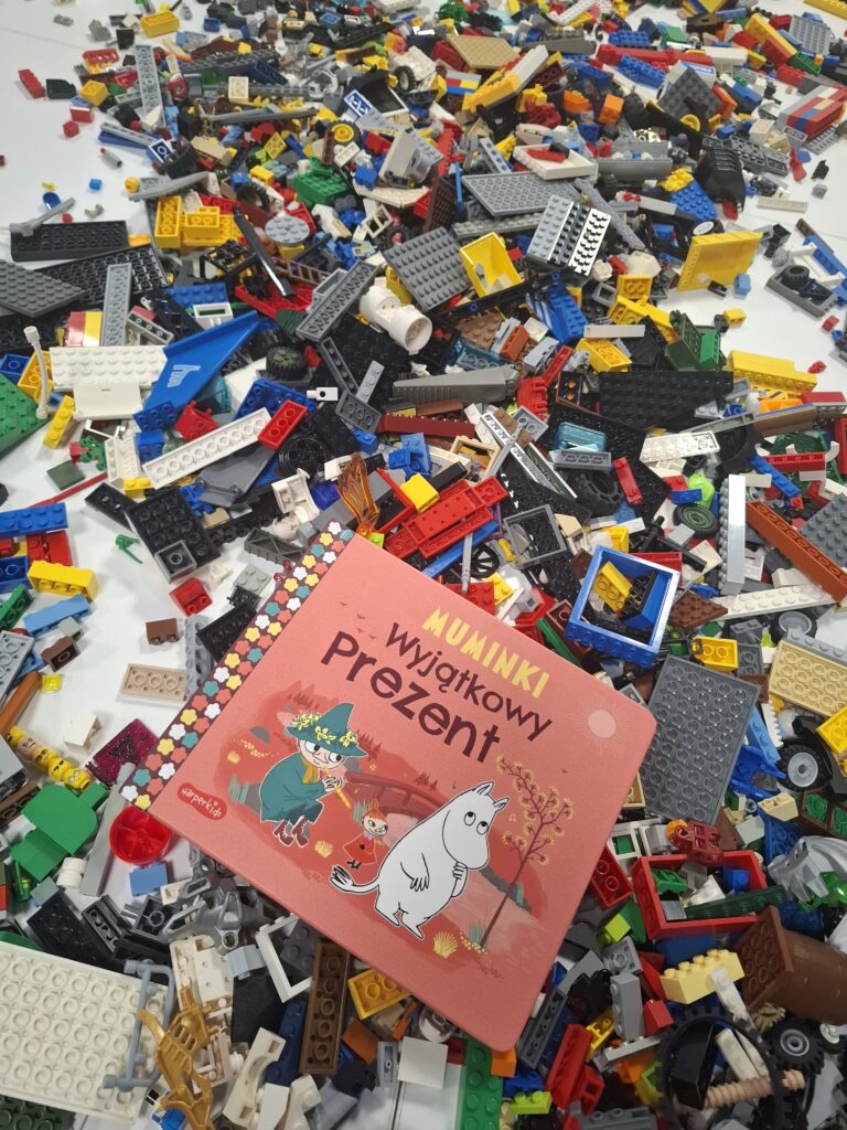 Na zdjęciu widać książkę „Muminki. Wyjątkowy prezent” położoną na stercie kolorowych klocków LEGO.
